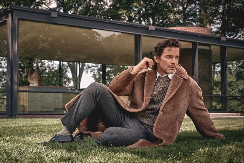 Matt Bomer lounges gracefully outdoors, clad in Todd Snyder's winter selection of a Mouliné cashmere crewneck, Italian alpaca balmacaan, flannel Gurkha trousers, a crisp Oxford shirt, and Paraboot Michael shoes.