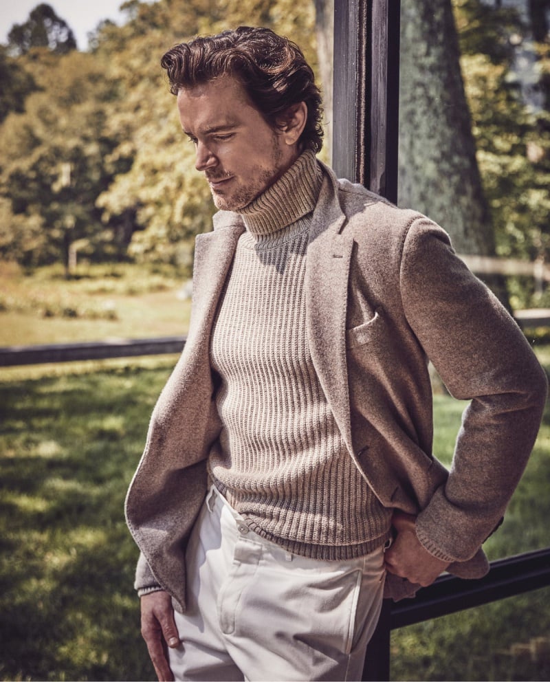 Leaning thoughtfully, Matt Bomer showcases a refined winter look in a fisherman stitch turtleneck and an Italian cashmere Madison sport coat, paired with relaxed-fit selvedge chinos.