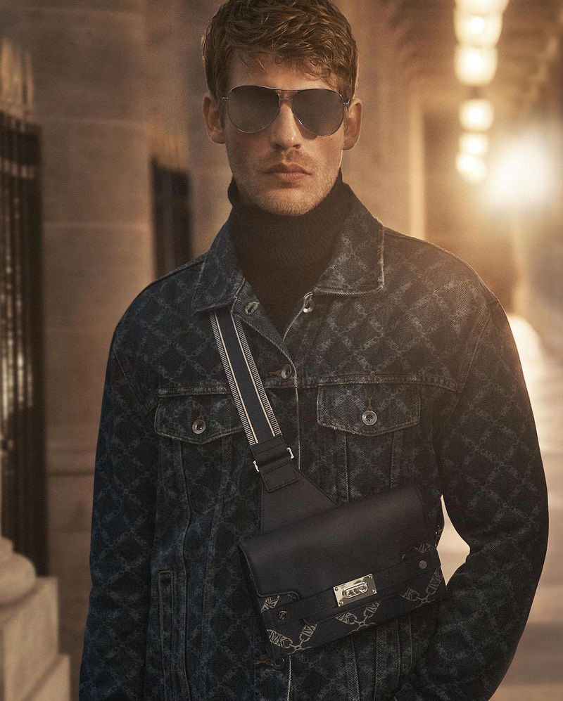 Baptiste Radufe models a stylish denim jacket paired with a black turtleneck and crossbody bag, bringing an air of casual cool to the Michael Kors Fall Winter 2023 collection.