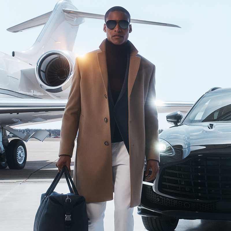 Malik Lindo strikes a commanding presence in a camel overcoat and black turtleneck from Michael Kors Fall Winter 2023 collection, ready for departure with luxury in tow.