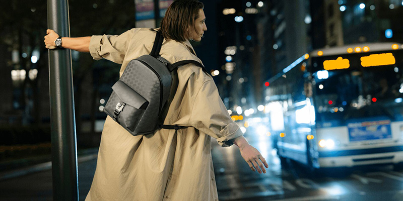 James Turlington captures the essence of city life at night, donning a classic trench coat and a stylish Montblanc backpack.