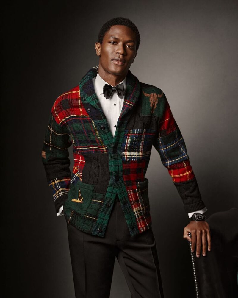 Hamid Onifade exudes debonair charm in a patchwork plaid shawl neck cardigan, paired with a crisp white shirt and bow tie.