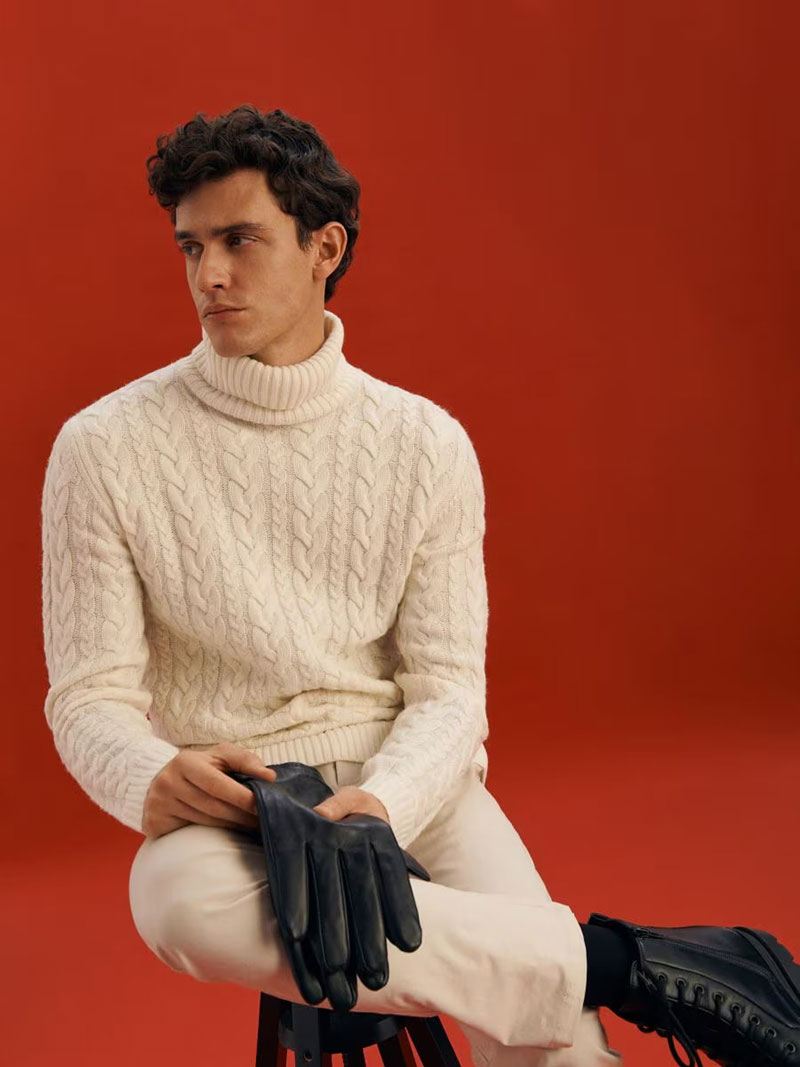 In a holiday-inspired setting, Xavier Serrano exudes a winter charm in a cream cable knit sweater complemented by off-white trousers. 