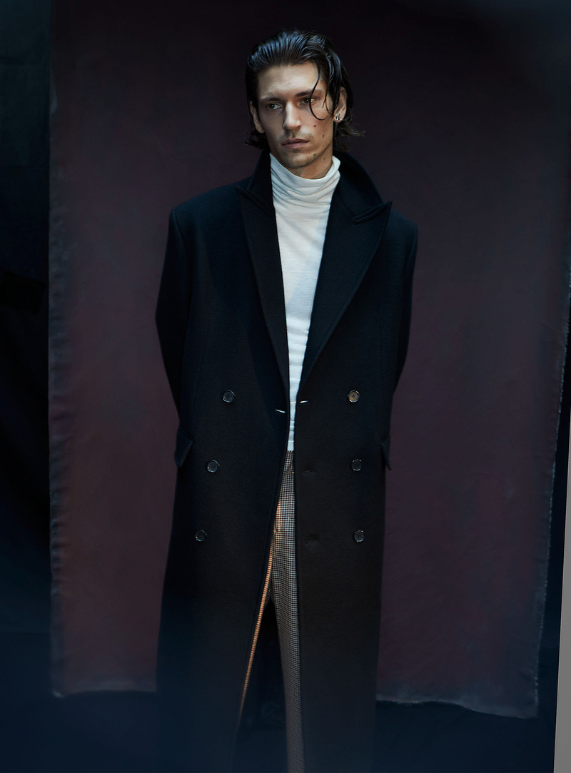 Donning a long double-breasted coat with a turtleneck and check trousers, Justin Eric Martin wears Filippa K.