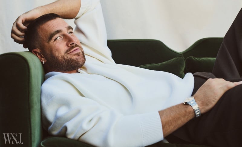 Travis Kelce lounges casually in a white sweater, juxtaposed with the rich green of a velvet chair, for WSJ. Magazine.