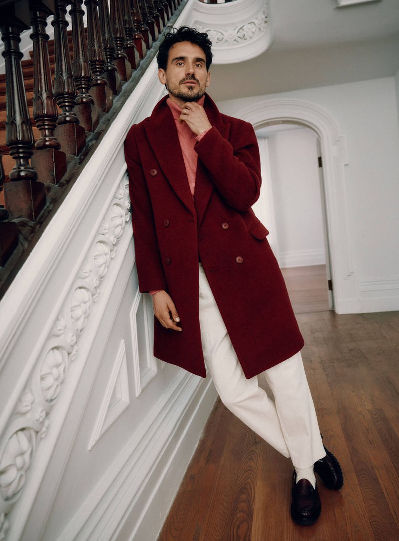 Arthur Kulkov embodies elegance in a double-breasted burgundy coat, complemented by a turtleneck and crisp white trousers.