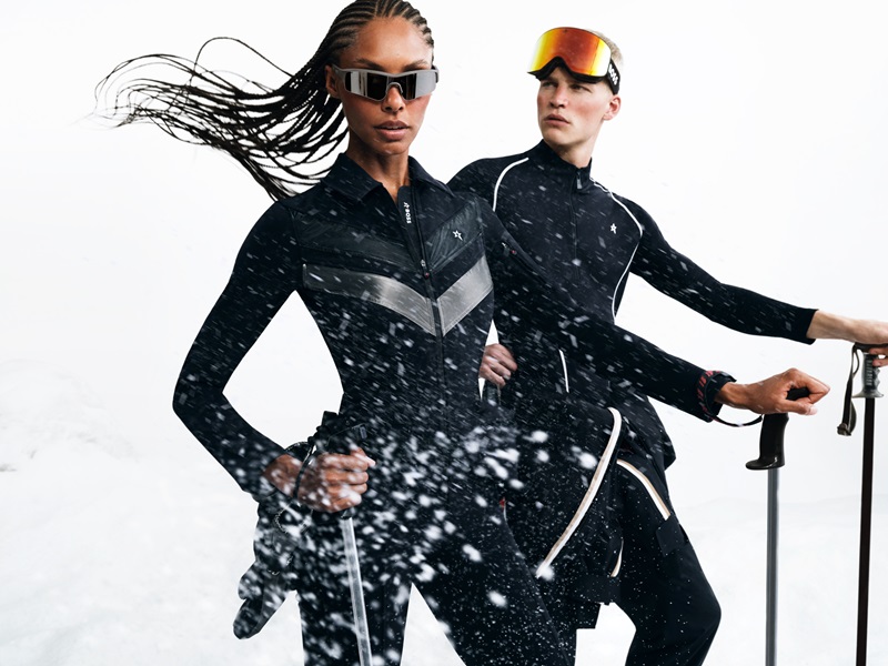 Ronja Berg leads with intensity in a sleek black BOSS x Perfect Moment ski jumpsuit, while Timo Pan, donning a similar outfit, looks on with focus.