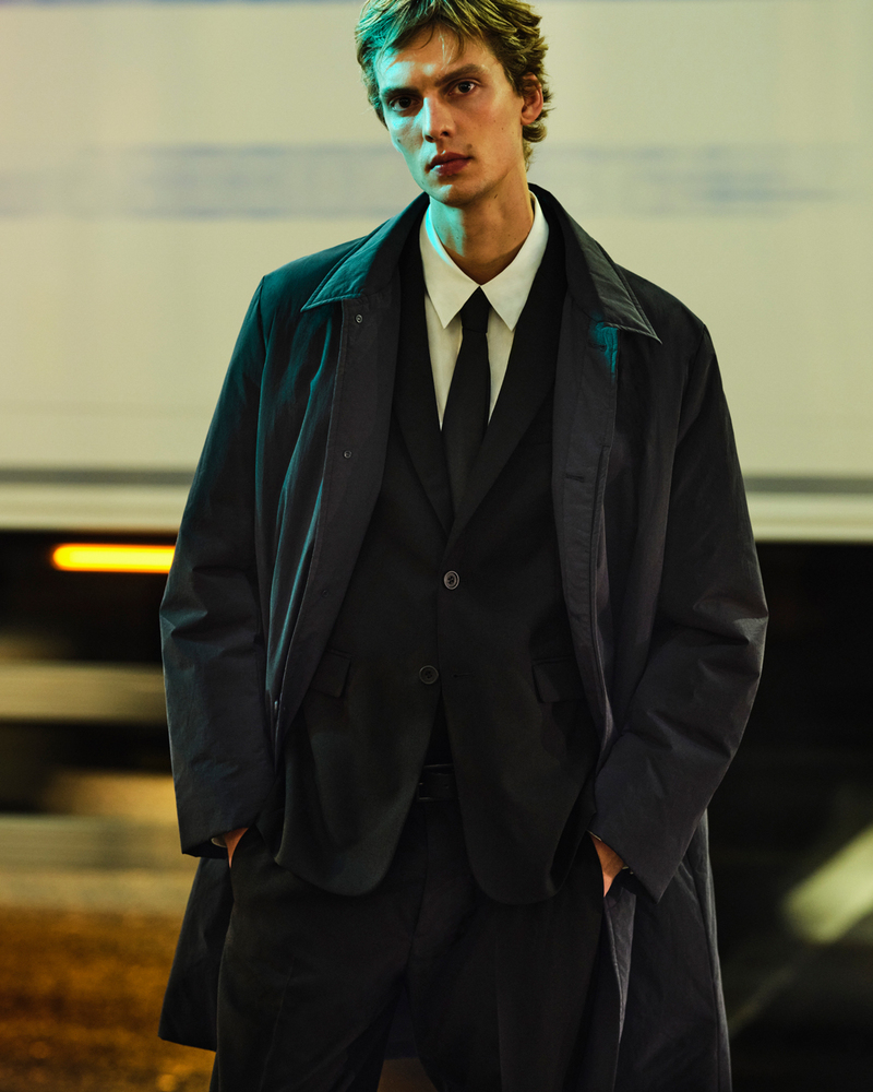 Leon Dame dons a COS suit with an unbuttoned overcoat against a backdrop of nocturnal urban lights.