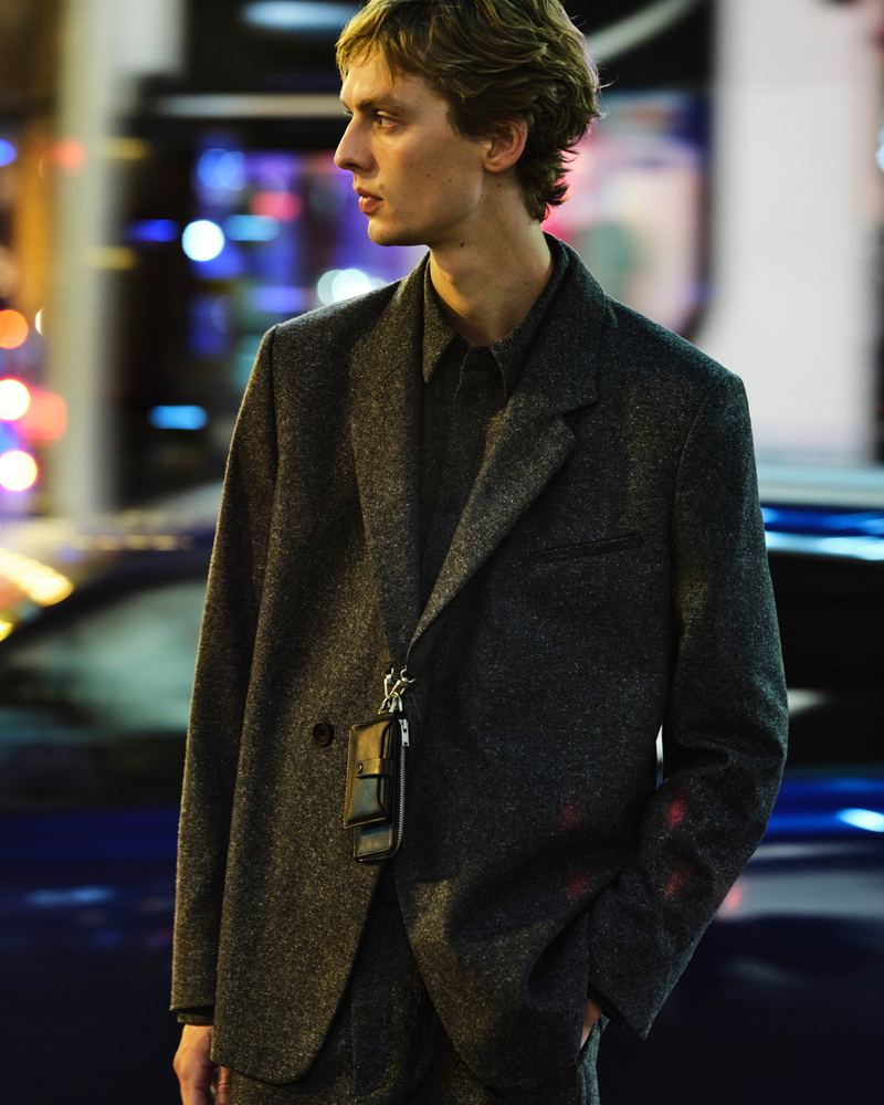 Model Leon Dame strikes a profile pose in a textured grey-tailored COS ensemble, complemented by a sleek leather accessory.