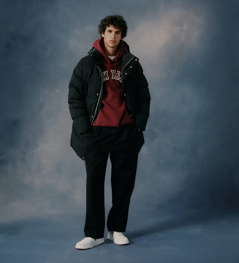 Francisco Henriques stands confidently in a GANT look, sporting a black puffer jacket over a maroon hoodie, with black trousers and white sneakers.