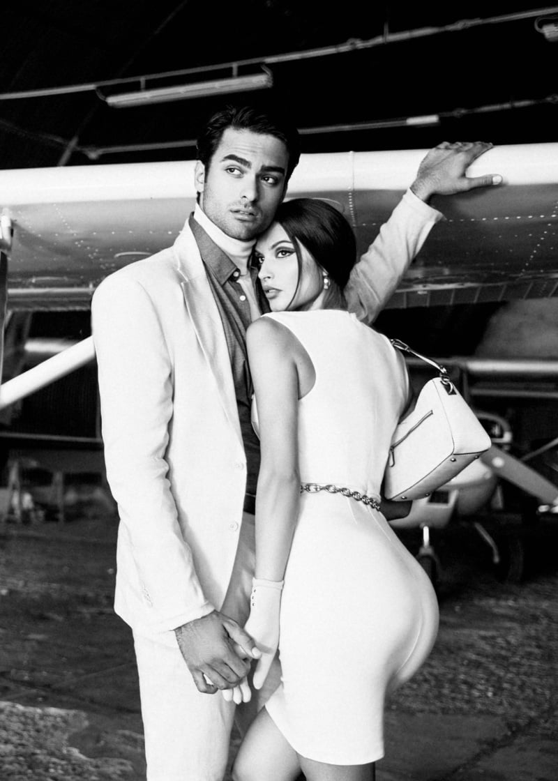 Matteo Bocelli and Oriola Marashi pose against an aircraft backdrop, capturing the essence of a chic getaway for the GUESS holiday 2023 campaign.