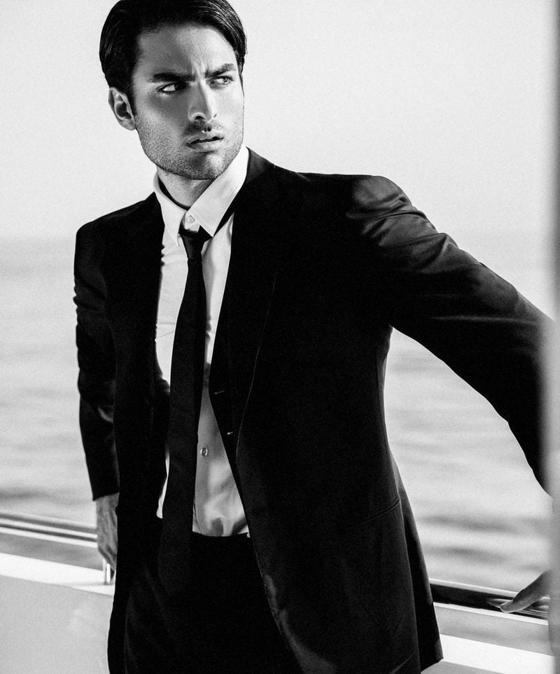 Matteo Bocelli casts a sharp, contemplative gaze, his silhouette framed by the yacht's sleek lines, donning a classic black suit that speaks to the understated luxury of the GUESS Holiday 2023 Campaign.