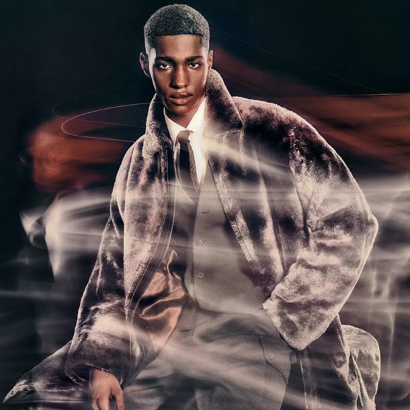 Diogo Gomes stands confidently in a Giorgio Armani faux fur coat, his pose blending with warm, ethereal swirls for the holiday 2023 campaign.