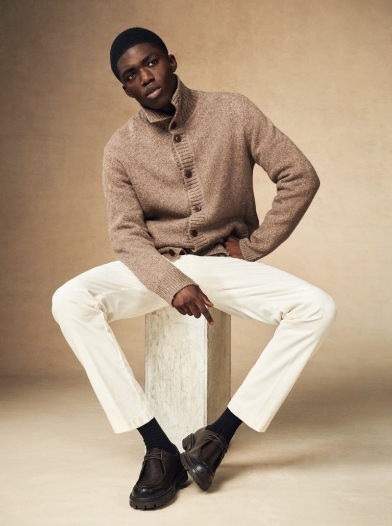 Sitting for a portrait, Jeremiah Berko Fordjour models an oatmeal-colored cardigan with crisp white pants and chunky dark loafers.