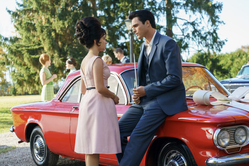 Jacob Elordi channels a vintage charm in a Valentino suit, leaning on a classic red car as he shares a moment with Cailee Spaeny, evoking a 1960s scene.