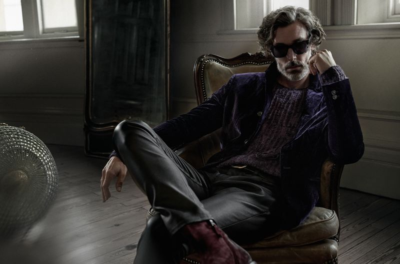 Richard Biedul exudes sophistication in a velvet blazer, lounging in a vintage armchair.