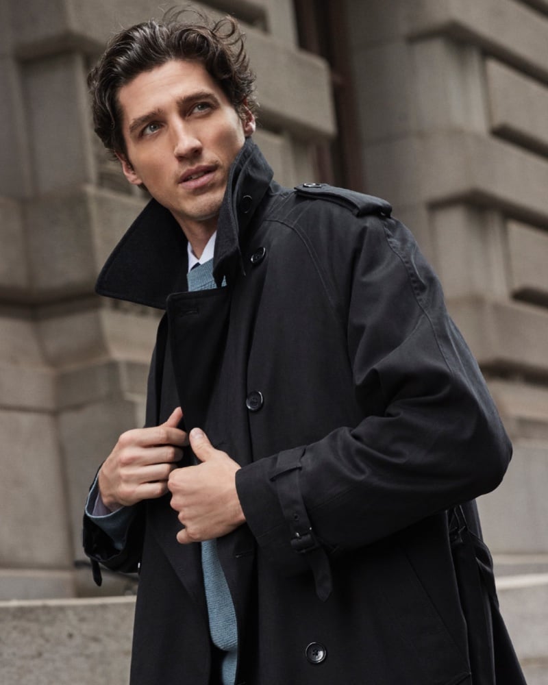 Ryan Kennedy models a classic black London Fog trench coat over a blue sweater.