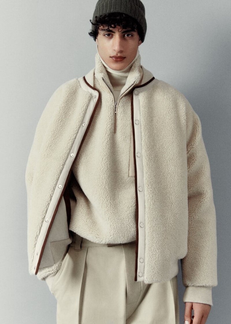 Yoesry Detre models an ivory shearling jacket with a turtleneck, trousers, and a knit beanie from Loro Piana's holiday 2023 collection.