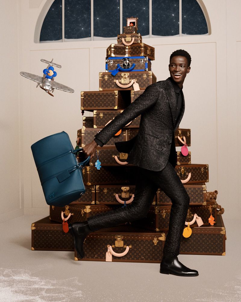 Ahmadou Gueye playfully strides past a pyramid of Louis Vuitton trunks, his joyous spirit as luxurious as the detailed suit he wears.