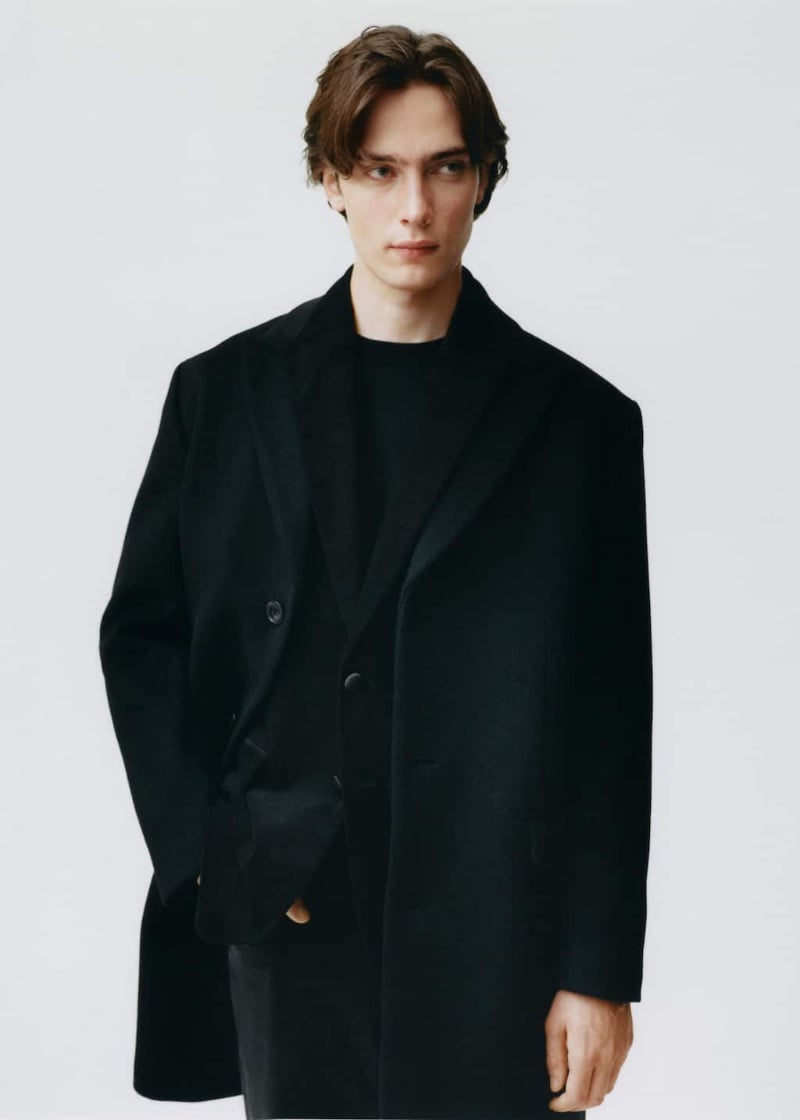 Showcasing an all-black outfit from Mango, Freek Iven wears a tailored coat over a suit.