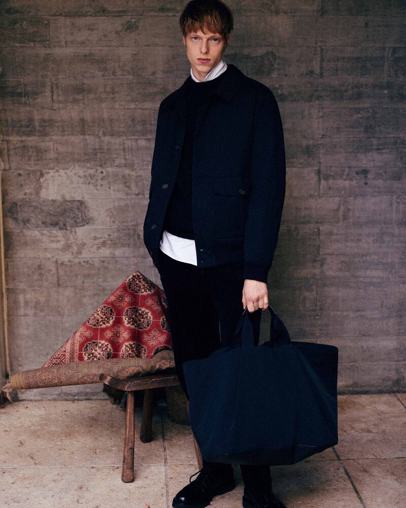 Joseph Uyttenhove exudes quiet confidence, wearing a chic navy jacket with a shirt, sweater, and a large matching tote.