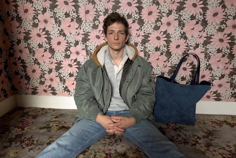 Mike Faist poses against a floral backdrop, his outfit completed with a parka for Loewe's pre-spring 2024 campaign.