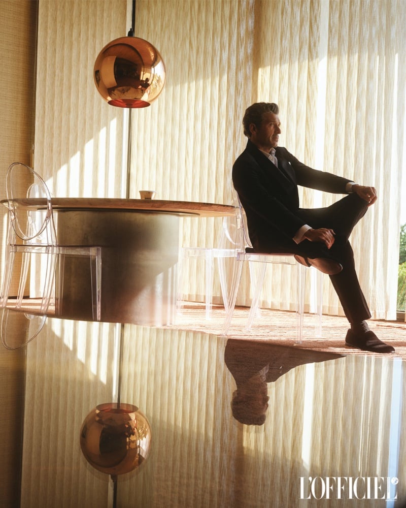 Patrick Dempsey seated elegantly against a backdrop of warm, golden sunlight in a modern interior for L'Officiel Argentina.