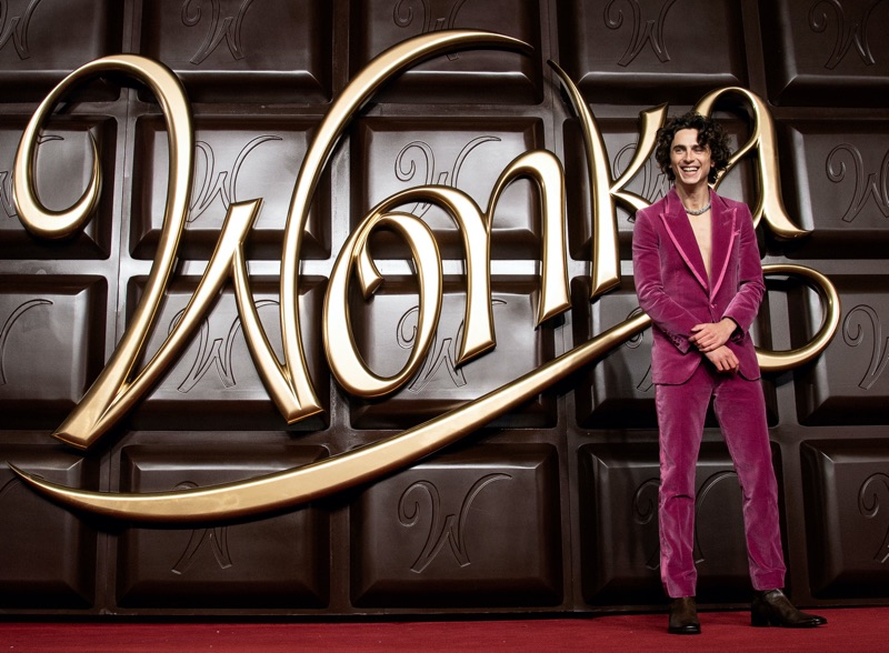 Timothée Chalamet captivates in a mauve Tom Ford tuxedo against the grand Wonka chocolate bar backdrop at the world premiere in London.