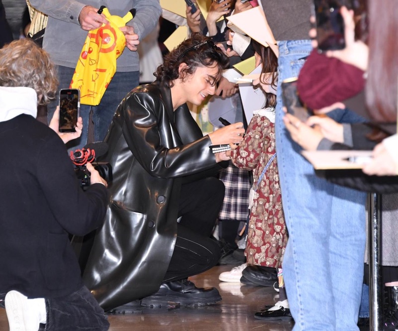Timothée Chalamet brings fashion-forward flair to the airport, greeting fans in a sleek Avellano latex coat.