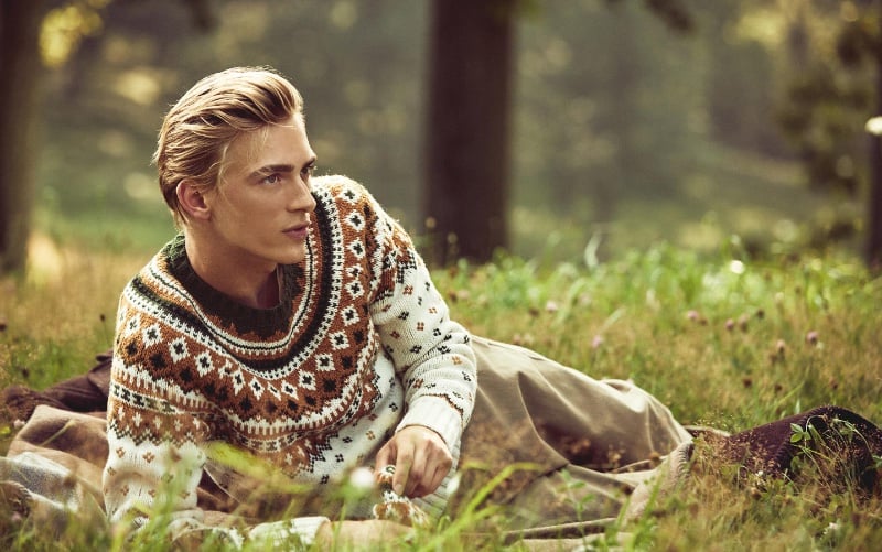 Model Dominik Sadoch relaxes in a pastoral setting, donning a Todd Snyder patterned knit sweater.