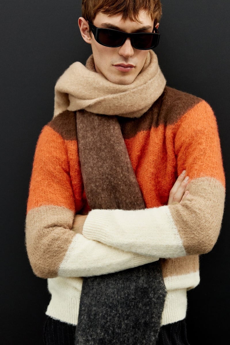 Kit Butler showcases a bold Zara knitwear piece with striking orange and earth tones, complemented by a plush oversized scarf.
