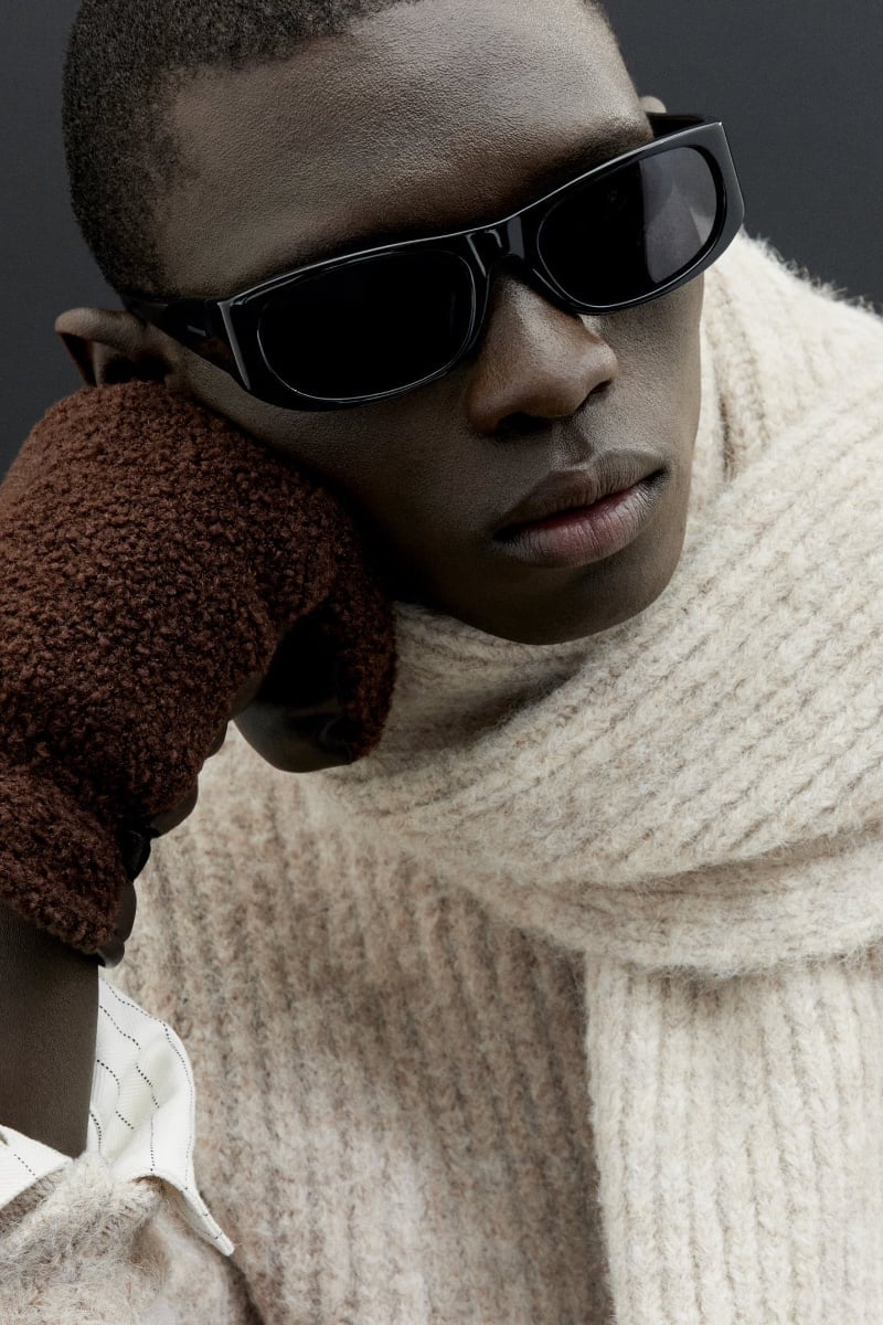 Capturing a contemplative mood, Fernando Cabral wears a chunky knit sweater with textured gloves and classic sunglasses.