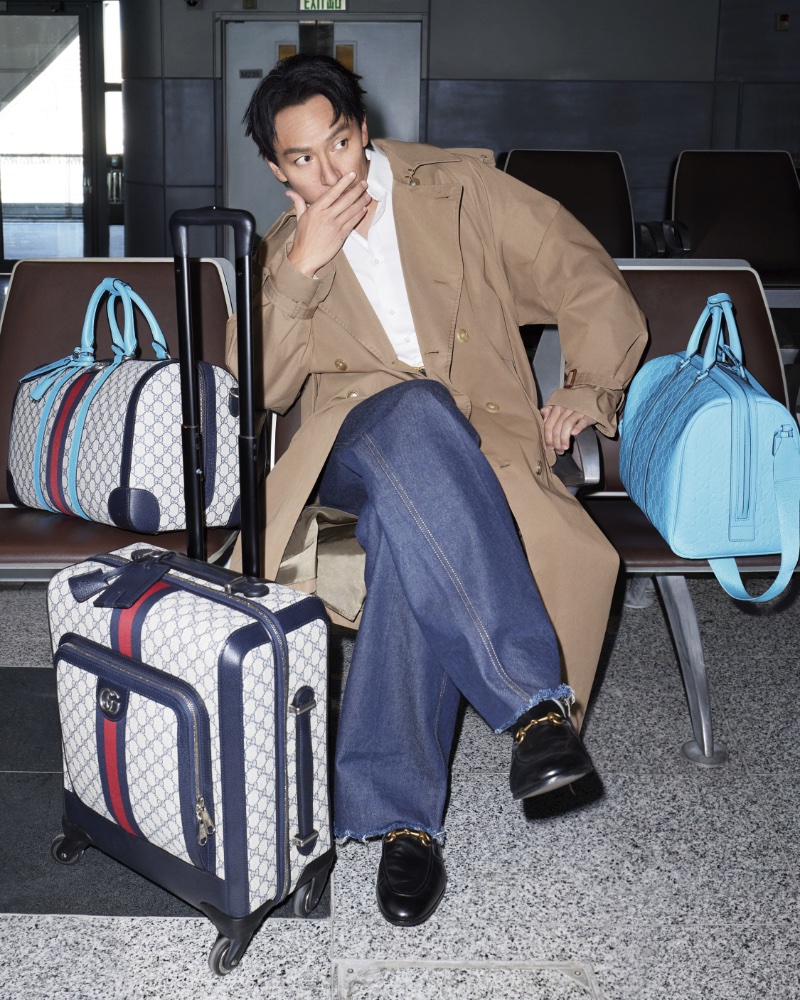 Sporting a trench with jeans, Chang Chen sits with the latest Gucci Valigeria travel pieces.