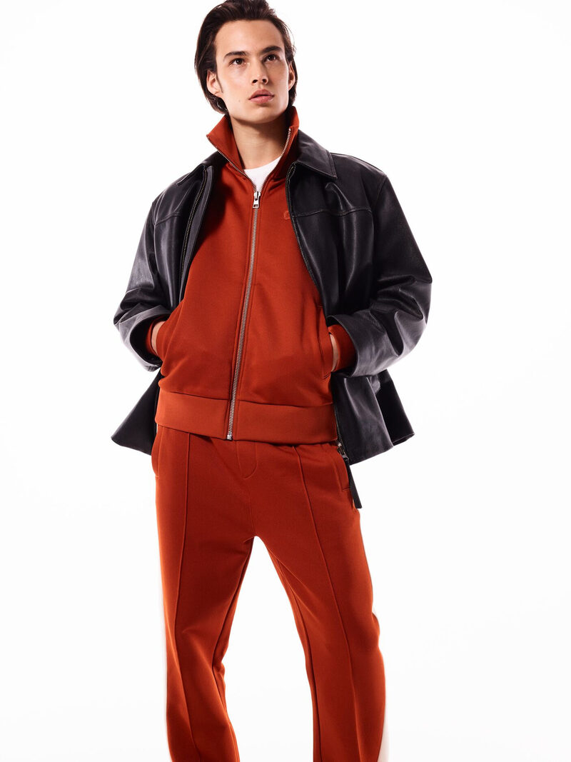 Louis Baines is captured in a striking ensemble from GANT's pre-spring 2024 collection, pairing a sleek leather jacket with a rich, rust-hued tracksuit.