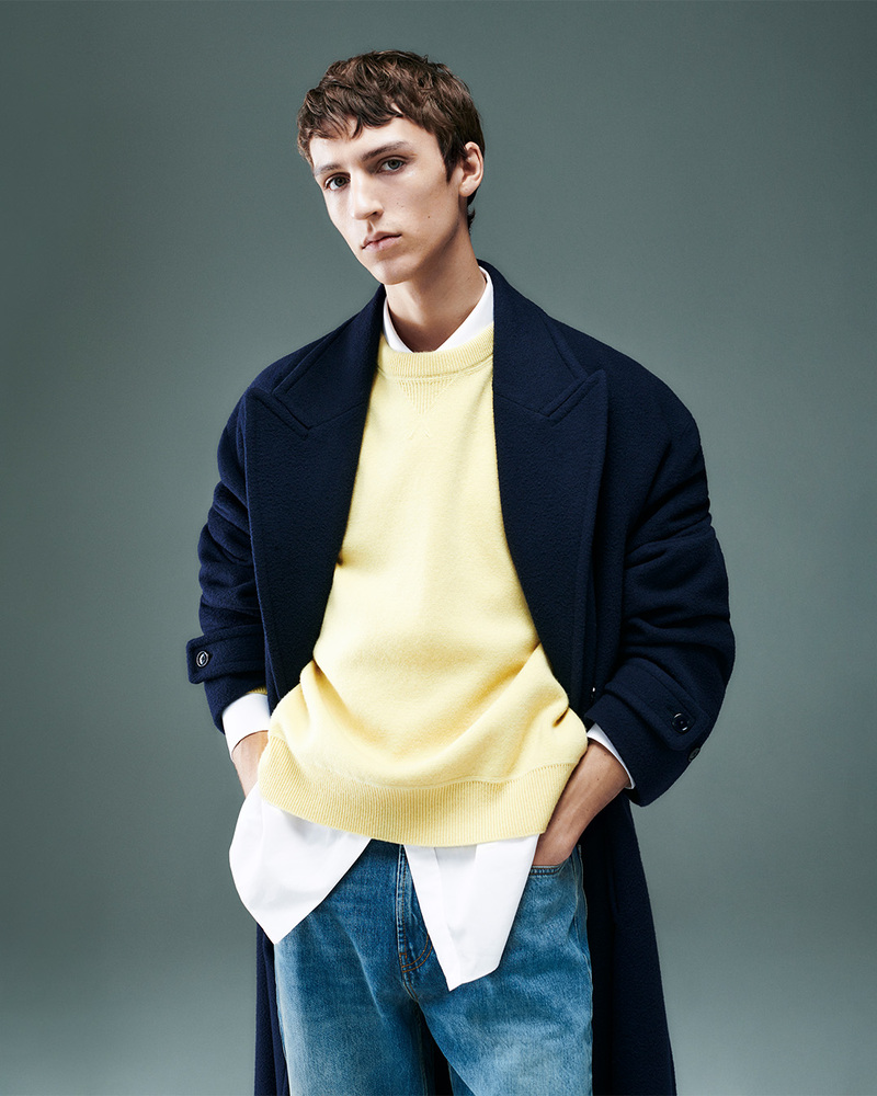 Layered in luxury, Saul Symon presents Mytheresa's Gucci selection with a navy overcoat over a vibrant yellow sweater, a fresh take for the 2024 collection.