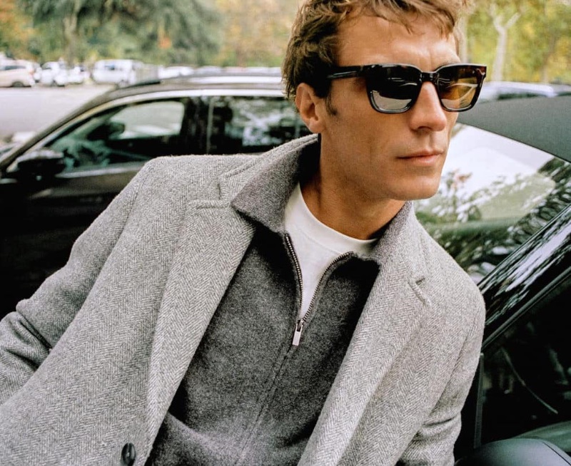Sporting shades of gray, Clément Chabernaud wears a Mango single-breasted coat over a cardigan with Bosco sunglasses.