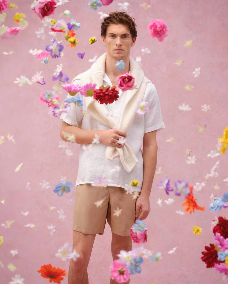 Model Luc Defont-Saviard stands amidst a cascade of spring blossoms in a spring outfit from Orlebar Brown.