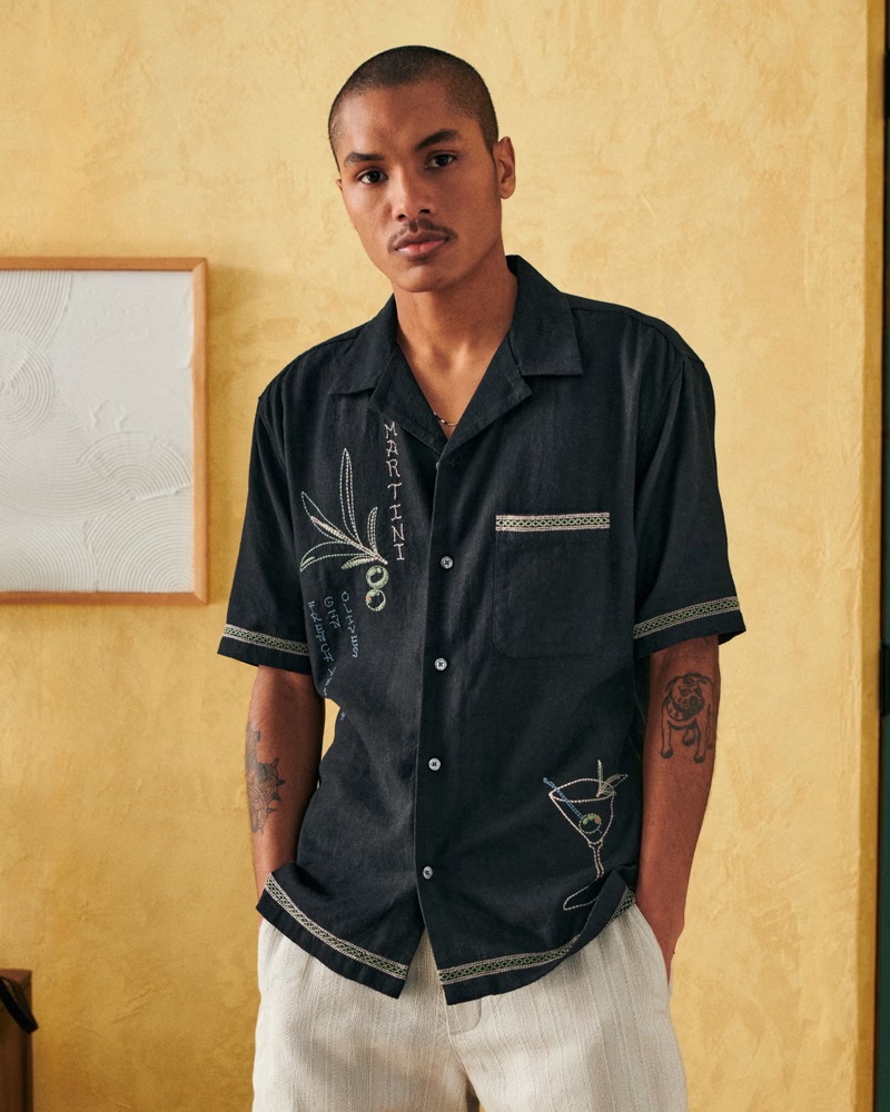 Sporting a black camp collar summer linen blend embroidered graphic shirt, Hector wears Abercrombie & Fitch.