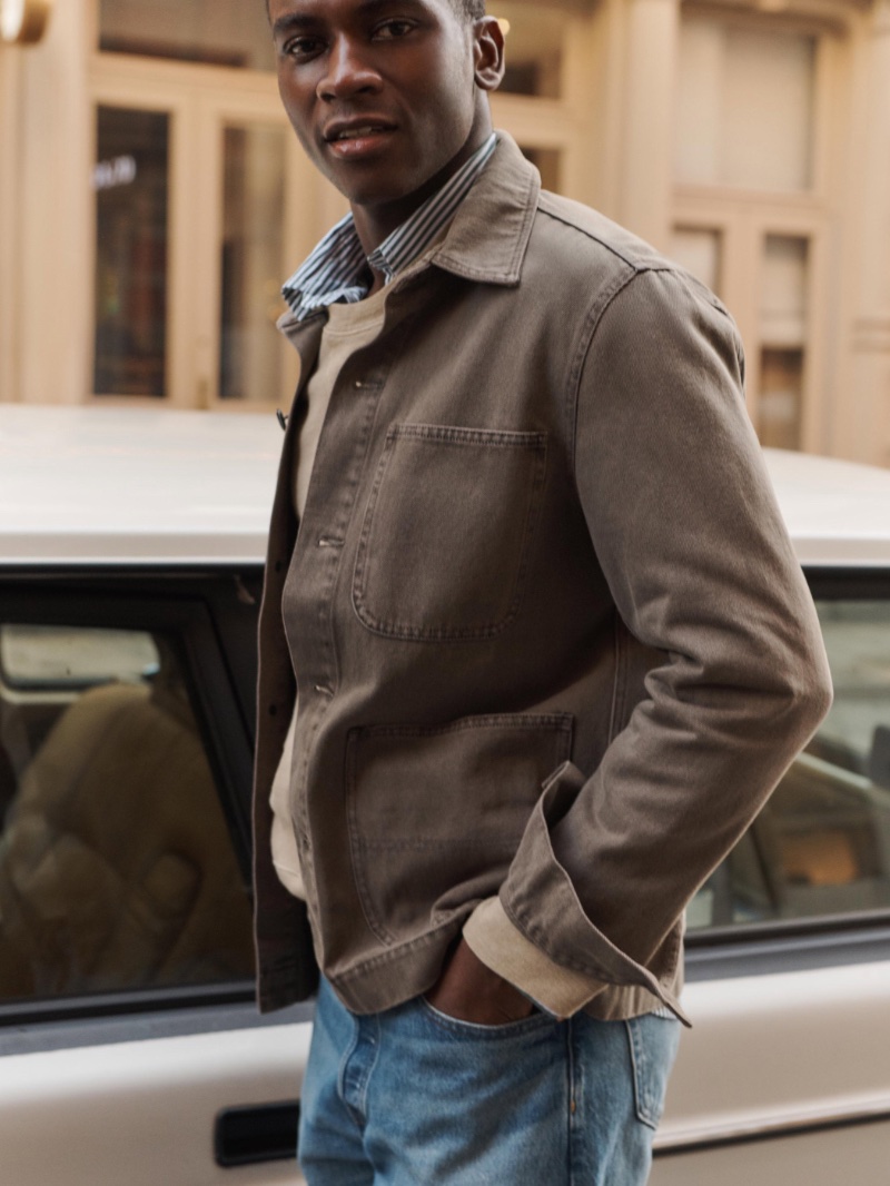 Idriss Marcus models Alex Mill’s garment dyed work jacket with a sweatshirt, striped shirt, and AM Original jeans.