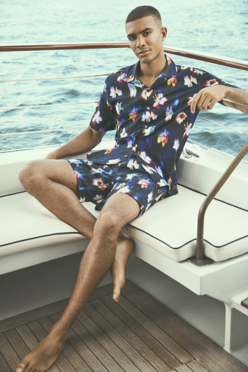 Addis Miller lounges on a yacht deck, clad in a floral print BUGATCHI shirt and shorts.