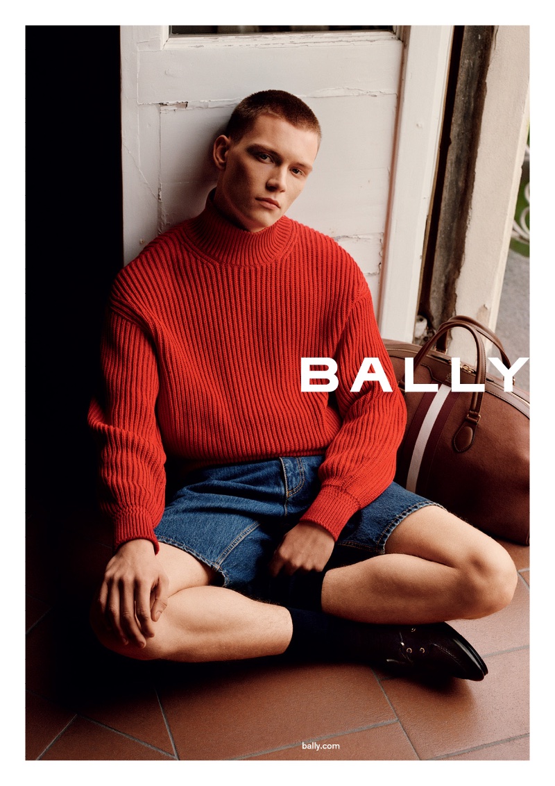 Will Woodward wears a ribbed red sweater with denim shorts for Bally's spring-summer 2024 campaign.