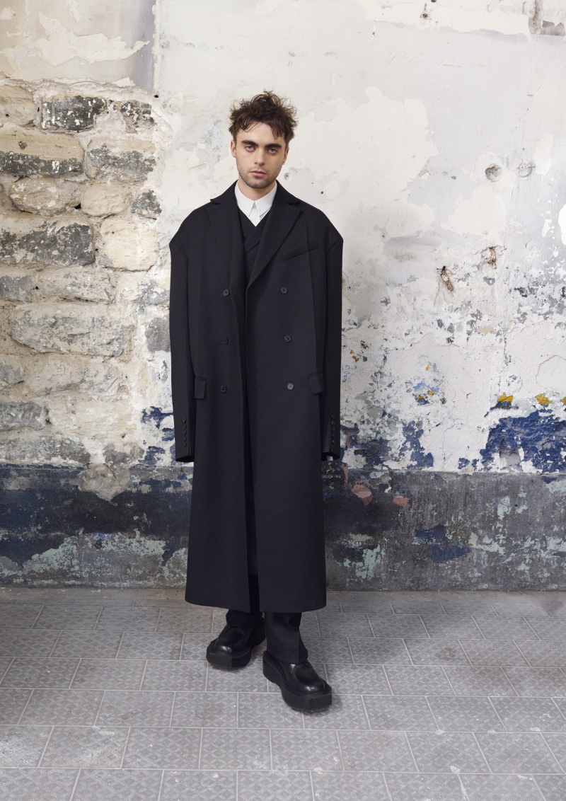 Against a rustic backdrop, Lennon Gallagher showcases an oversized black coat from the H&M x Rokh collection. 