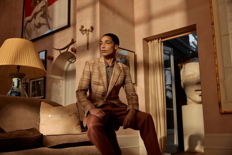 Luke Cousins sits poised in a classic checkered blazer and earth-toned trousers from the Huntsman spring-summer 2024 collection.