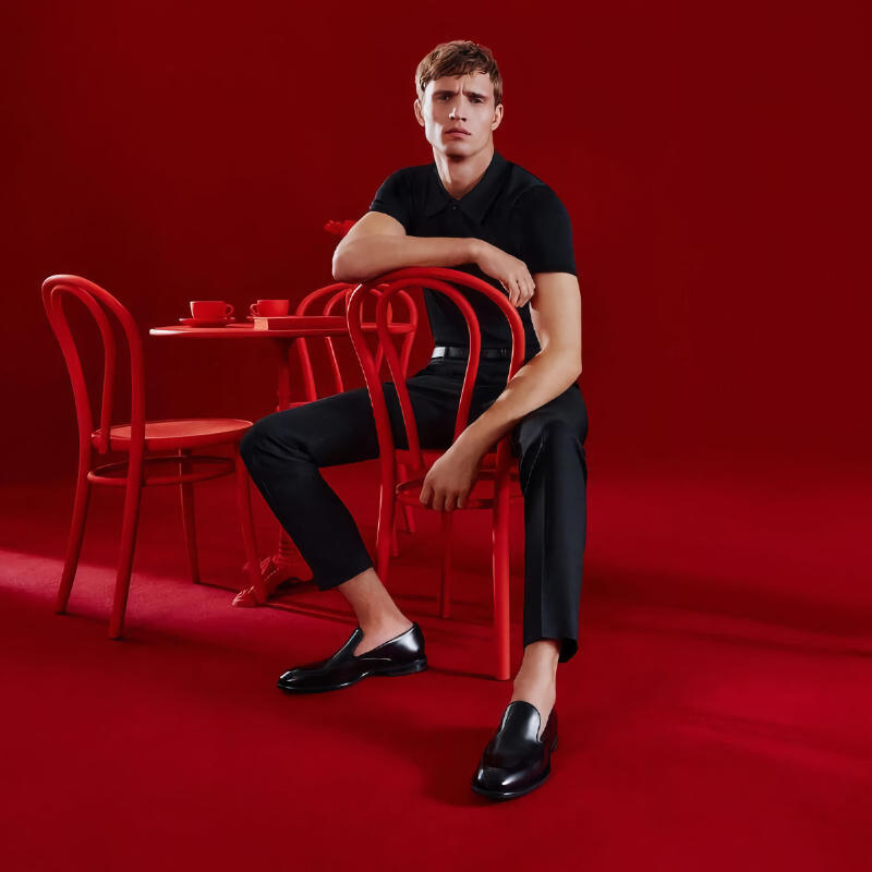 Set against a striking red backdrop, Julian Schneyder dons chic black attire with polished loafers for LLOYD's spring-summer 2024 campaign.