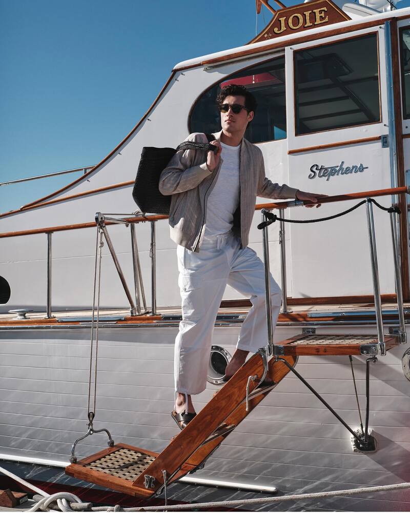 Donning light-colored neutrals, Adam Sattrup sports an Italian linen varsity jacket, linen jersey t-shirt, garment-dyed cargo pants, and Nomad suede-leather crossover sandals. 