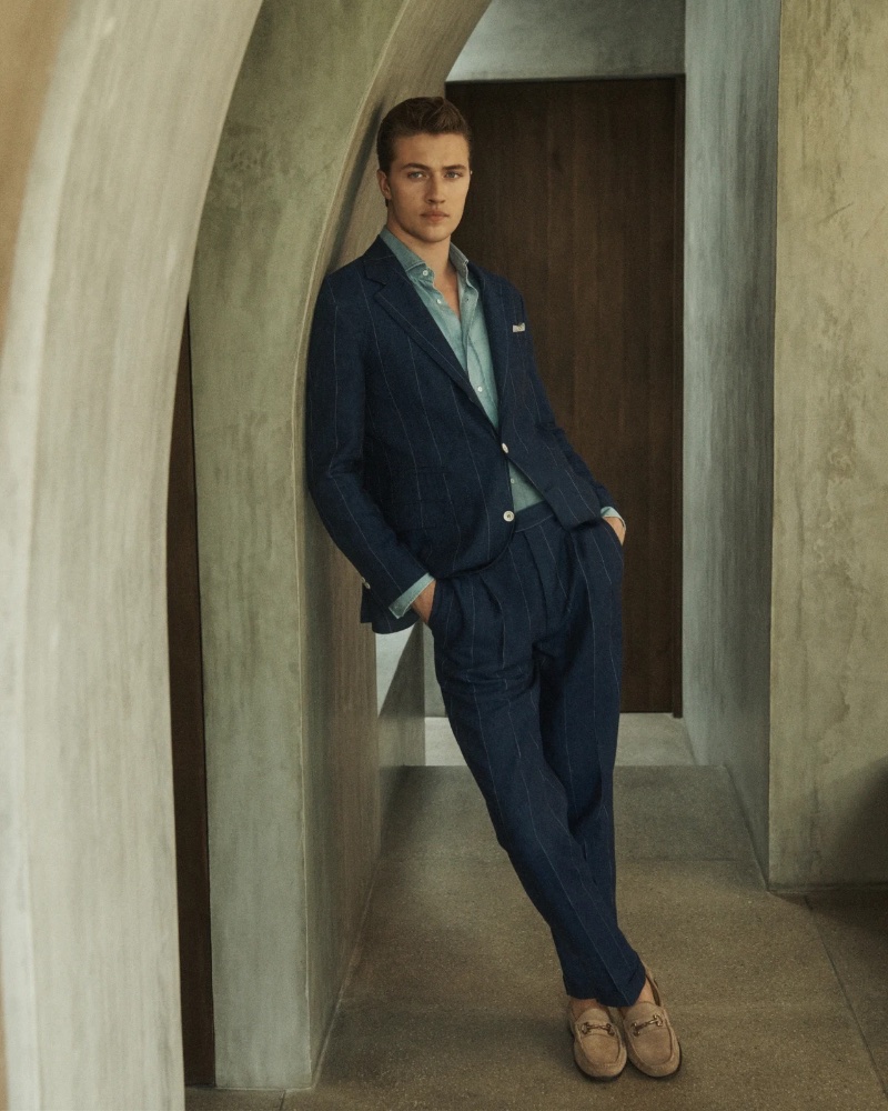 Captured in a serene architectural space, Lucky Blue Smith dons a navy pinstripe suit from the Brunello Cucinelli spring-summer 2024 collection.