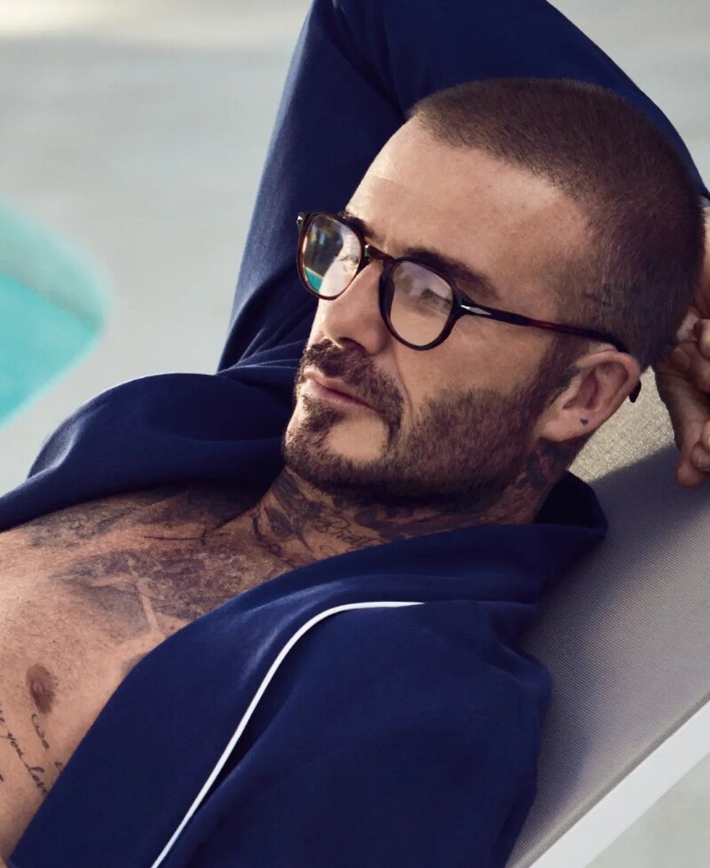 David Beckham relaxes poolside, donning glasses with a navy robe in his spring 2024 eyewear campaign.
