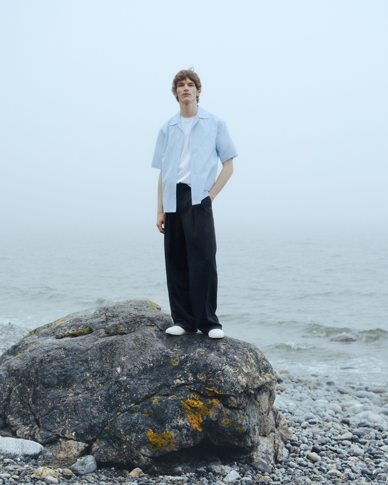 Poised on a seaside rock, Erik van Gils stars in Filippa K's summer 2024 campaign.