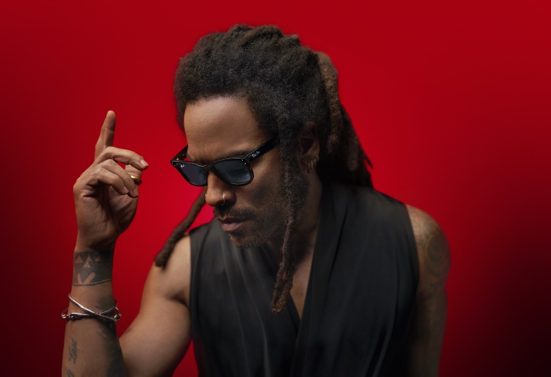 Lenny Kravitz poses in a vibrant red setting, his Ray-Ban Reverse sunglasses taking center stage. 