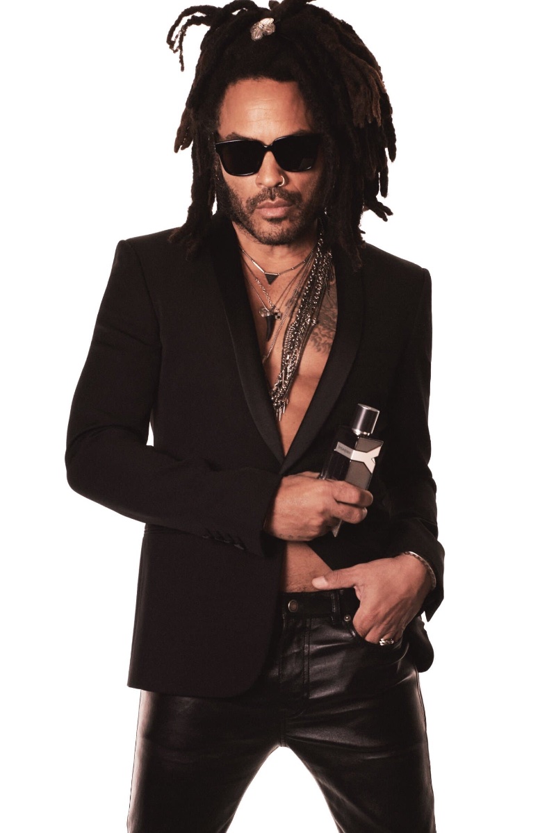 Lenny Kravitz wears a blazer and leather trousers, holding the Y Elixir by Yves Saint Laurent bottle.